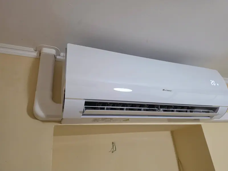 Működő beltéri egység sárga falon, mellette fehér csőtakaró elem
